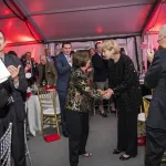 Georgie Shockey shaking hands with OSU President Johnson standing in a crowd of people applauding in a hall with white ceiling and red lighting