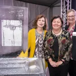 Georgie Shockey standing in the middle of two ladies with hands clasped in font of her standing next to an ice sculpture