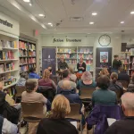 Two people seated talking with an audience in a book store.