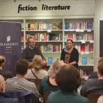 Two people seated talking with an audience in a book store.