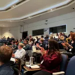 A crowd sitting in an auditorium clapping for Aaron Wilson.