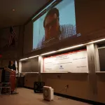 Tom Darrah presenting via Zoom in big screen.