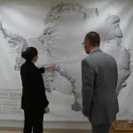 Heidi Roop showing Jason Cervenec a location on a very large Antarctic map on the wall.