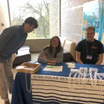 Two people sitting at the registration table and one standing.