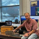 Jamey Stutz sitting on a table with his hand on a rock.