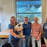 Four people posing for the photo, the very left  person is holding a dog.