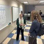 A person presenting a poster to another in an open space. 