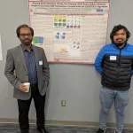 Two people posing with a poster in the middle.