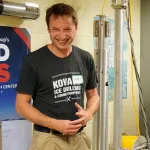 Person wearing a KOVA Ice Drilling and Coring Equipment t-shirt smiling in a laboratory setting.