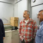 Three individuals conversing in a laboratory with "ice" sign visible in the background.