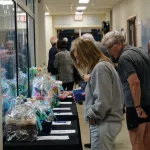 Several people standing at a table examining items in a silent auction at an indoor event.