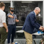 Four people interacting with virtual reality headsets indoors. One individual is being assisted by another to adjust their headset while.