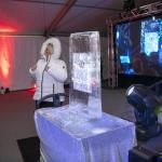Andrea Bowlin, OSU Advancement, in a white short puff Eskimo jacket standing to the left of an ice sculpture on a table in a room with white walls and red spotlight coming from the ground on the wall