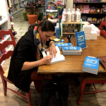 Heidi Roop seated at a table signing books.