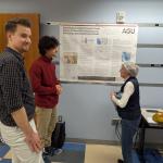 Tw people discussing a poster while a third looks toward the camera.