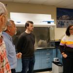 People in a laboratory setting, listening to a  person speaking.
