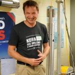 Person wearing a KOVA Ice Drilling and Coring Equipment t-shirt smiling in a laboratory setting.
