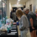 Several people standing at a table examining items in a silent auction at an indoor event.