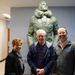 Three people standing beside a large statue of Admiral Byrd at a public facility.