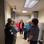 A group of people standing in a corridor, listening to a person in the center speaking.